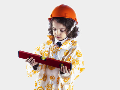 在一件雨衣，持有建设水平的可爱卷发的男孩生成器。工头在橙色建筑头盔。灰色的背景
