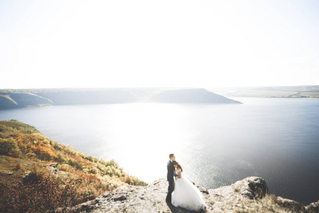 婚礼情侣接吻和拥抱蓝色海边的岩石上