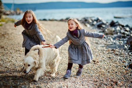 两个小的孪生姐妹散步和在海滩上的狗