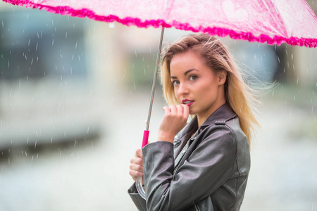 年轻漂亮的女人，与粉红色的雨伞，在雨和大风。秋天的天气在伞的女孩