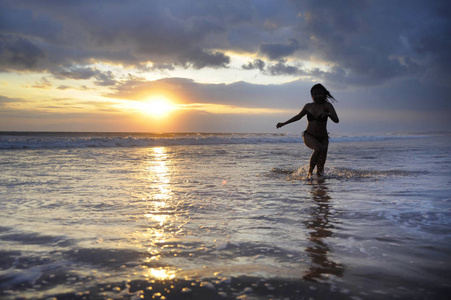 年轻美丽的轮廓和的亚洲女人运行自由和快乐，在日落海滩在巴厘岛玩