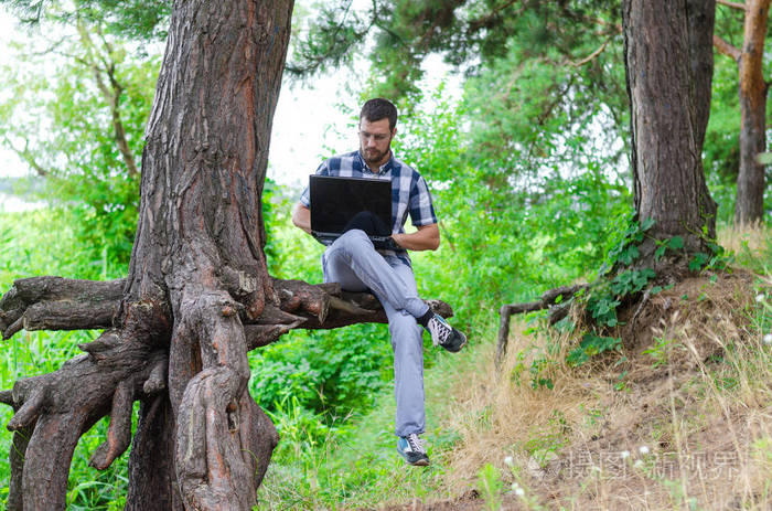 年轻男人放松与笔记本电脑坐在公园 工作和 r