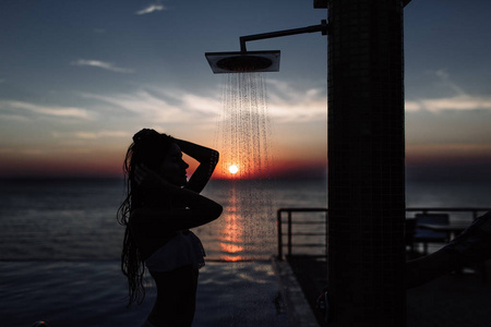 一个漂亮的女孩与一个完美的身材的沐浴在夕阳中海和游泳池的轮廓照片