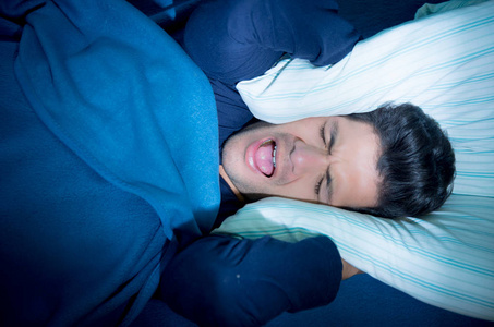 英俊的年轻男子在床上痛苦失眠和睡眠障碍,覆盖耳朵里的塞了一个枕头