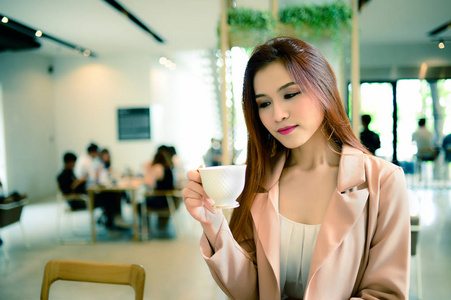 美丽的女人拿着一杯咖啡在她手中的画像模糊背景咖啡店，她在早上，复古风格喝咖啡
