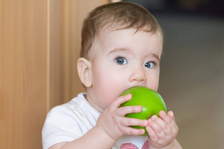 用一个大的绿色苹果的小小孩。孩子咬苹果带着惊讶的表情