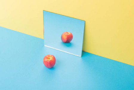 孤立在靠近镜子的黄色背景的蓝色桌子上的苹果