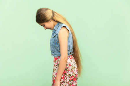 悲伤的十几岁的女孩，惩罚独自一人在绿墙的侧面图。室内影棚拍摄
