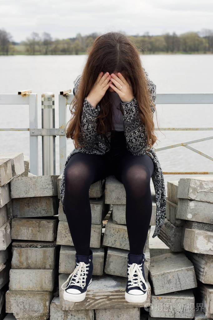 伤心的女孩坐在河边的混凝土砌块