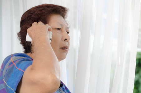 亚洲高级女人在家里窗户附近使用电话