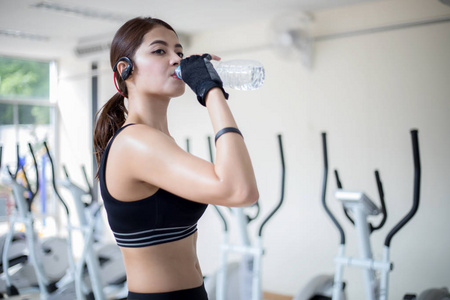 运动型女人亚洲饮水后在健身房里锻炼。适合