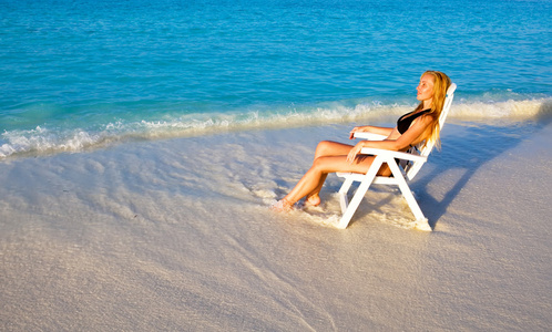 年轻漂亮的女人在沙滩椅上，放在海洋里