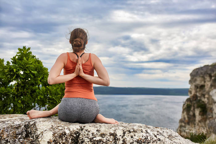年轻女子在瑜伽姿势蹲在河上方的岩石后视图