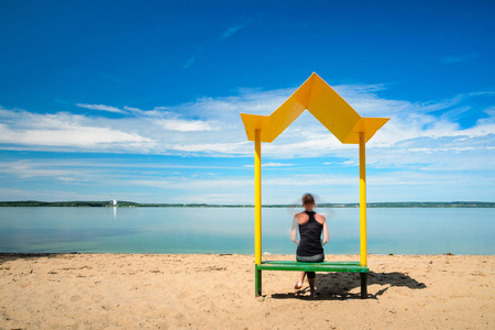一个女孩坐在一个黄色的金属长凳上的剪影与太阳在海滩上的树冠。放松和娱乐的概念。长时间曝光