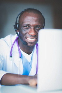 年轻的男医生在诊所桌上使用计算机时戴耳机的画像。医生