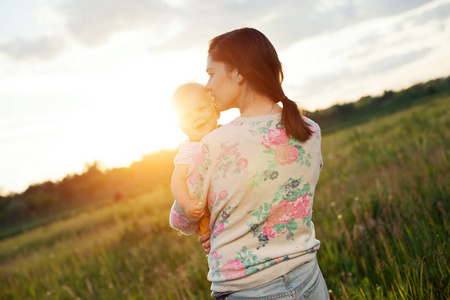 快乐妈妈亲吻她的孩子在公园里在户外母亲亲吻新生儿母亲亲吻婴儿父亲
