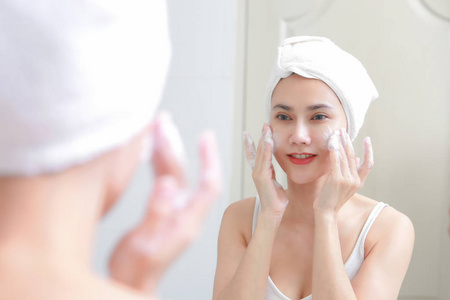 亚洲女人清洗脸上的皮肤享受自己与泡沫 cleansi