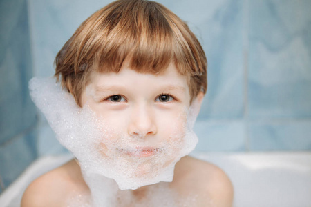 一个孩子在洗澡，他脸上的泡沫的画像。一个快乐的男孩在浴室里洗澡。孩子们脸上的肥皂泡沫