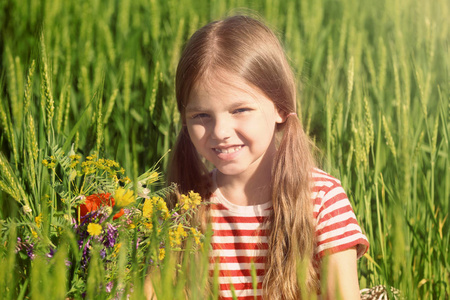 小女孩用束野花在绿色的田野