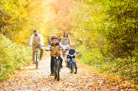 年轻的家庭，在暖和的衣服，在秋天公园骑自行车