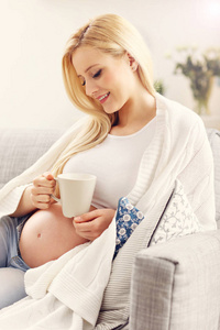 幸福的怀孕女人坐在沙发上休息