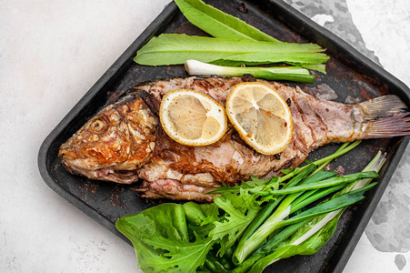 油炸鲫鱼柠檬和绿叶生菜香料腌制的烤的鲫鱼照片