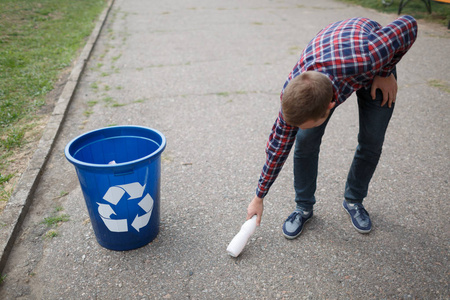 一个年轻的男子捡塑料瓶，把它扔到绿色回收箱。一个好公民关心性质