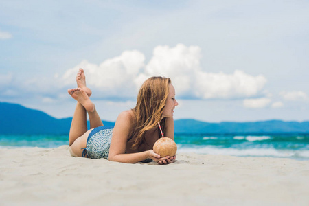 在海滩上喝椰子牛奶的年轻女子