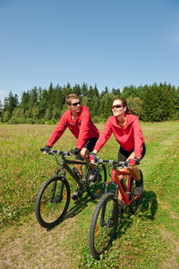 年轻夫妇骑着山地车在春天的草地上
