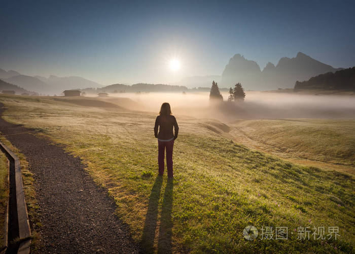 年轻女人站在雾的田野朝着太阳升起