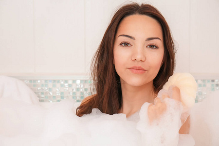 美丽的女人在带有泡沫的浴缸中休息