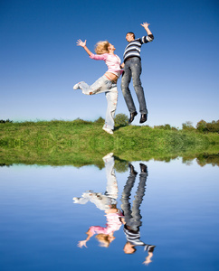 快乐的年轻夫妇，在一片绿色的草地上空跳