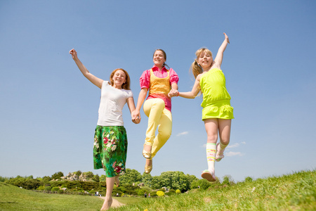 快乐妈妈和跳跃的绿草地上的两个女儿