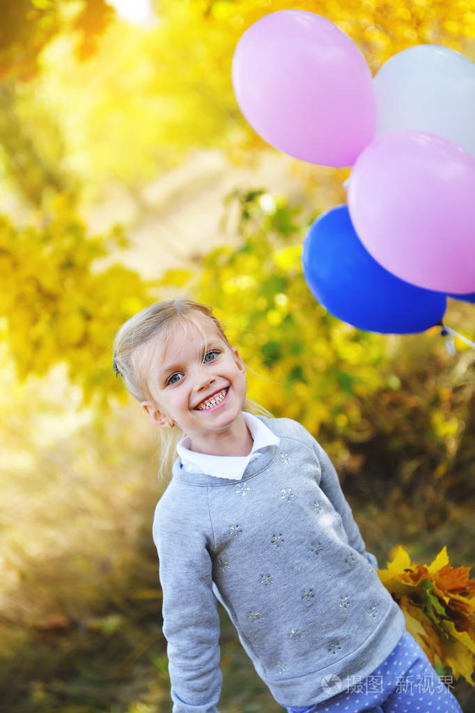 快乐小女孩，站在一个公园附近黄色枫叶在秋天里的气球