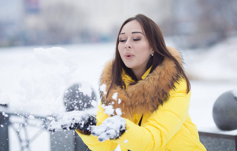 快乐美丽的年轻女子在一天的冬季吹雪花从她的手