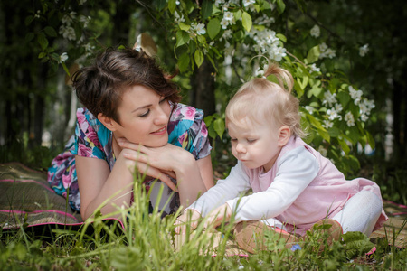 母亲和女儿在公园和苹果的树与白花玩得开心