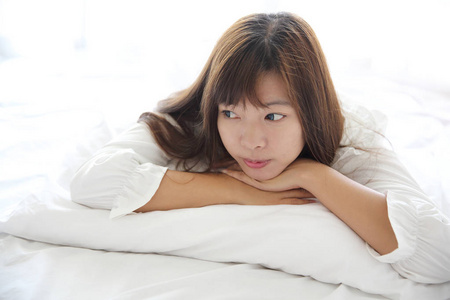 亚洲的年轻女子用枕头在白色的房间里醒来