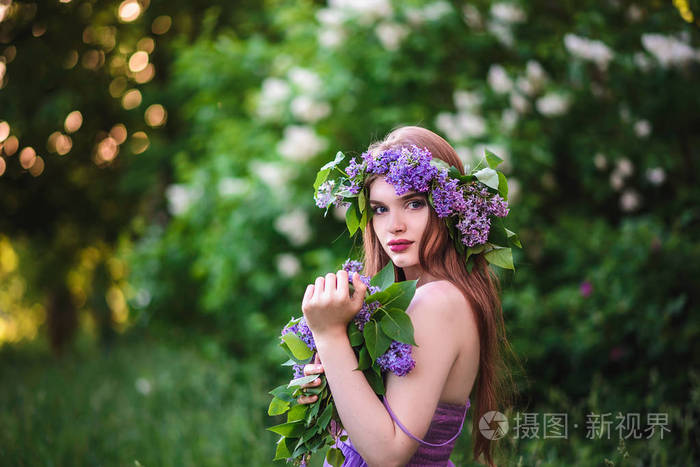 花环幸福的年轻女人在春天紫丁香的公园女孩与丁香在他头上的花环女孩
