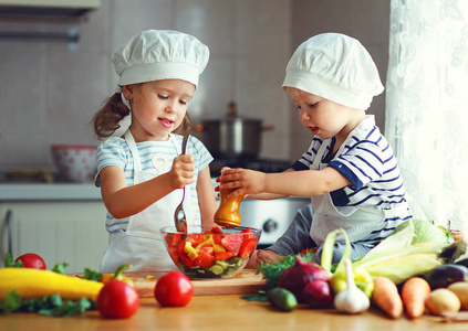 健康的饮食。快乐的孩子们准备在厨具的蔬菜沙拉