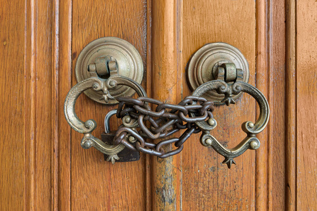两个古董铜华丽的门门环在一个古老的木制华丽的门关闭与生锈的锁链和挂锁特写