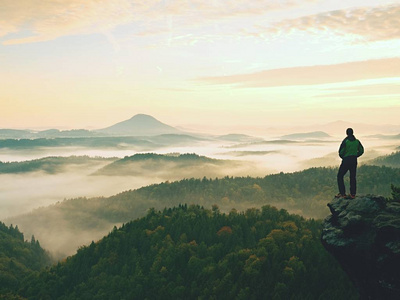 徒步旅行者站在岩石公园的砂岩山顶上, 看着薄雾蒙蒙的清晨山谷照片