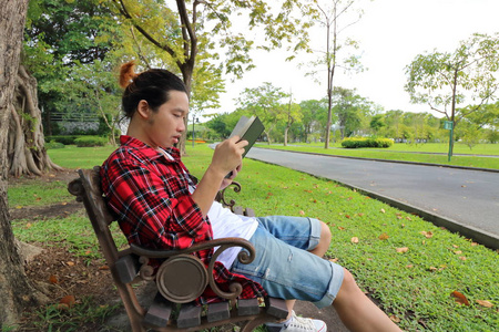 年轻的年轻人在美丽的户外公园的长凳上读一本书的肖像。广角拍摄