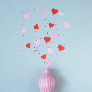 粉红色和红色纸心与花瓶的蓝色背景。顶部视图