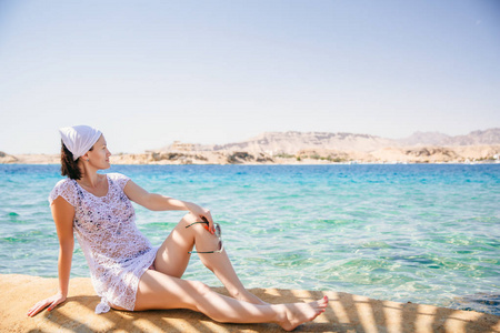 一个穿着白色长袍的女人正坐在前面的海边, 她正在看一个岛