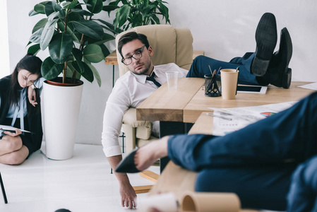 工作过度的生意人睡在办公室与脚在桌上