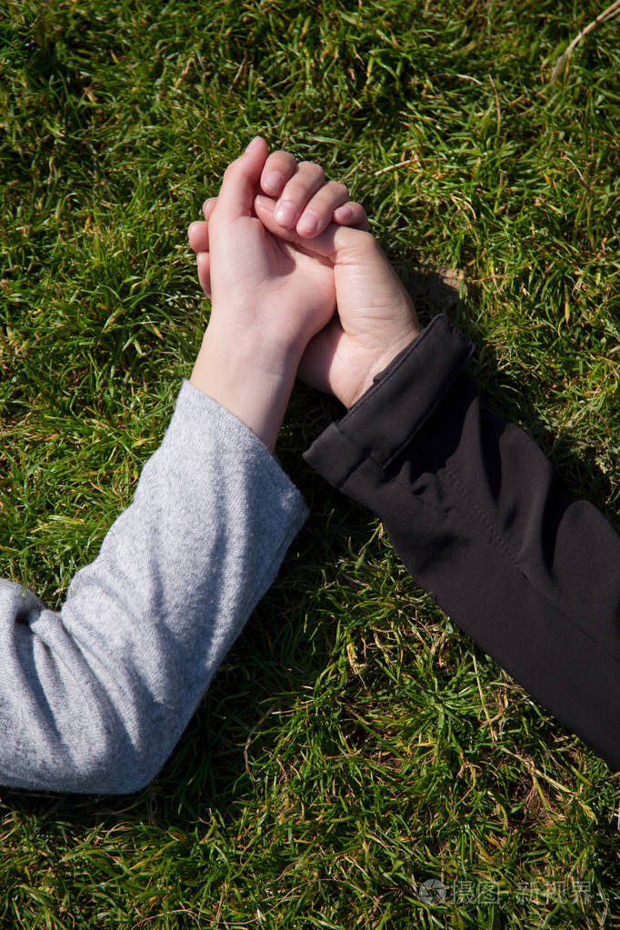 两个女手, 母亲和 saughter 握着彼此躺在草丛中的手