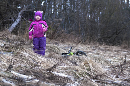 可爱的小女孩站在附近骑自行车在冬季森林