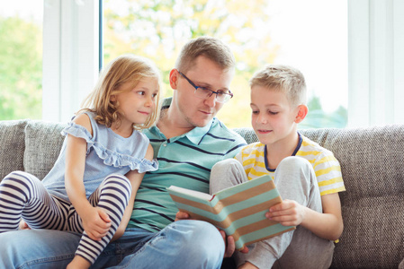 年轻快乐的父亲读书与逗人喜爱的孩子在家