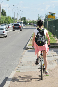 女孩骑自行车沿着繁忙的高速公路后方视图