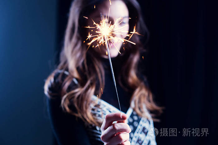 快乐的女孩微笑着手里拿着闪闪发光的烟花女孩在背景故意迷离庆祝新年